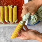 filling being pushed into manicotti pasta shells.