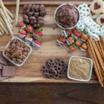 pretzels, caramels, strawberries, and cookies on a dessert board.