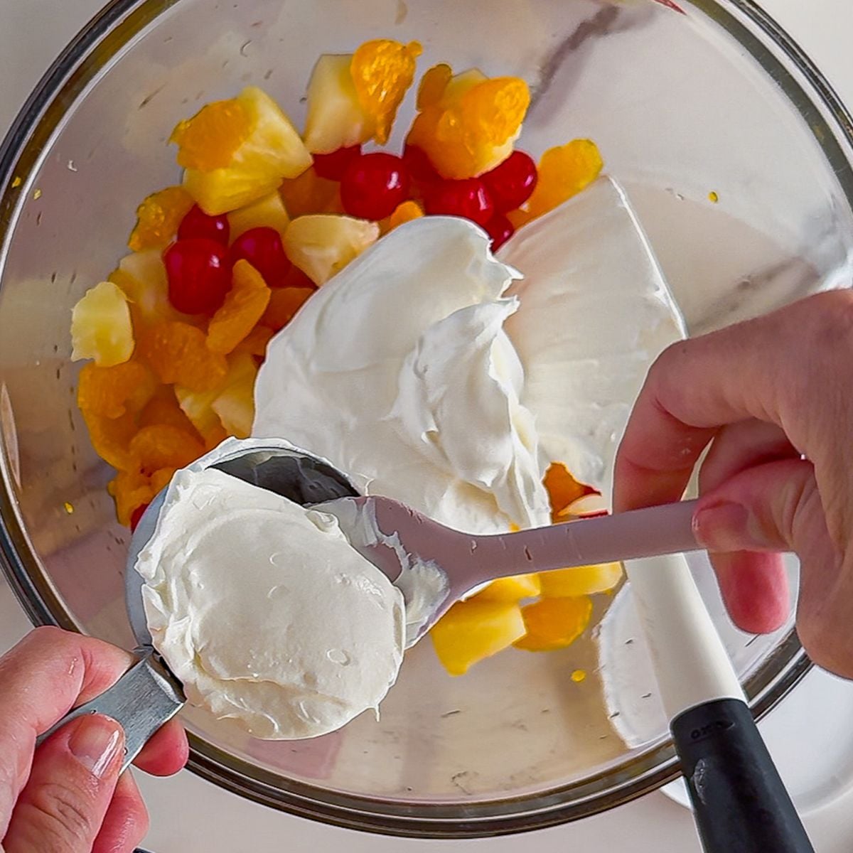 Mixing in the cool whip into the ambrosia salad.